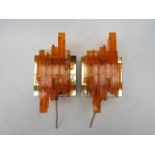 A pair of wall lights, with brass coloured metal holders and textured orange lucite diffusers.