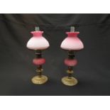 A pair of gilt metal and cranberry overlayed opaque glass oil lamps