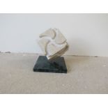 A carved marble cube sculpture on green marble plinth, unsigned.