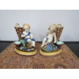 A pair of Wedgwood Circa 1871 spill vases with cherubs seated next to wine baskets holding glasses,