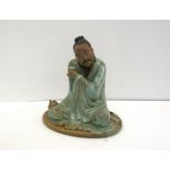 A 20th Century Oriental part-glazed terracotta figure of a man kneeling on a rush mat holding a cup,