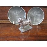 A chrome bronze mascot of a dog and two glass dishes depicting The Spirit of Ectasy