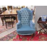 A wingback armchair in blue velour upholstery with button back