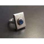A dress ring in rectangular mount centre set with sapphire framed by diamond chips