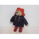 A Paddington bear in blue duffel and red Wellies,
