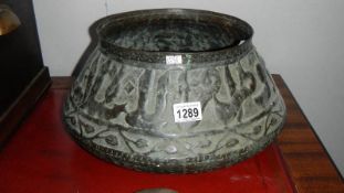 An early 19th Century large Islamic copper bowl decorated with embossed calligraphy and leaves.