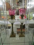 A pair of Victorian 'peg' oil lamps with brass columns, glass fonts and cranberry glass shades,