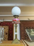 A brass Corinthian column oil lamp with pink glass floral decorated font and Sherwood's burner