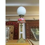 A brass Corinthian column oil lamp with pink glass floral decorated font and Sherwood's burner