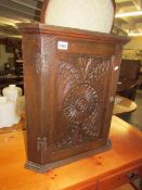 An oak corner wall cabinet with carved door.