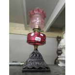 An oil lamp with cranberry shade and font