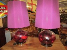 A pair of red glass table lamps with shades.