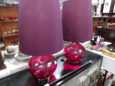 A pair of red glass table lamps with shades.