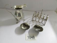 A silver toast rack, a silver cream jug and a pair of silver shell salts, all hall marked,