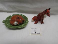 A Beswick fox and another glazed pottery sleeping fox on a leaf.