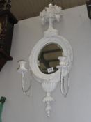An oval mirror in painted frame with candle sconces.