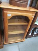 A pine 3 shelf cabinet with glass door.