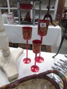 A set of 3 graduated red glass candleholders with gold coloured decoration.