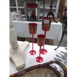 A set of 3 graduated red glass candleholders with gold coloured decoration.