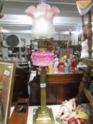 A brass Corinthian column oil lamp with pink glass font.