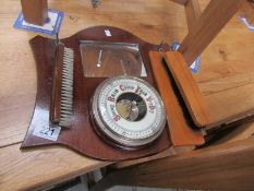 A barometer on wooden back plate with brushes.