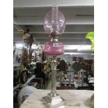 A silver plated Corinthian column oil lamp with cranberry glass font and shade.