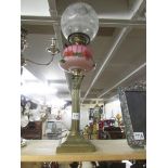 A brass Corinthian column oil lamp with floral pink font.