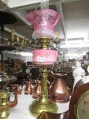 A brass oil lamp with pink glass font and cranberry etched glass shade.