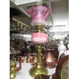 A brass oil lamp with pink glass font and cranberry etched glass shade.