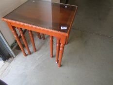 A dark wood stained nest of 3 tables with protective glass tops.