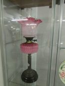 A brass oil lamp with pink glass font and shade.