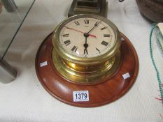 A brass ship's clock on wooden back plate,.