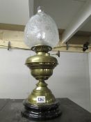 A brass oil lamp with pot base, complete with shade and chimney.