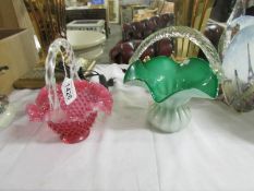 A green glass basket with clear rope handle and a cranberry glass basket.