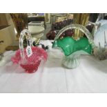 A green glass basket with clear rope handle and a cranberry glass basket.