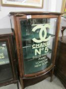 A bow fronted display cabinet with Chanel No.5 advertising to door.