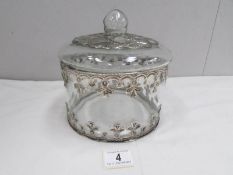 A glass cookie jar with white metal decoration.