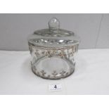 A glass cookie jar with white metal decoration.