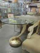 A circular glass top table on gilded base with elephant tusk style support.