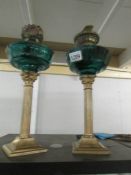 A pair of Corinthian column oil lamps with odd burners and green glass fonts, 1 font a/f.