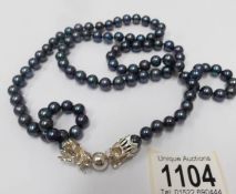 A black (navy?) pearl necklace with silver dragon fastening (37" long).