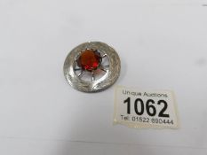 A Scottish circular brooch with orange centre stone in a silver coloured metal.