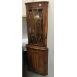 A medium/dark stained corner cupboard with astragal glazed top