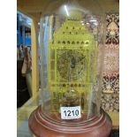 A brass skeleton clock under glass dome.