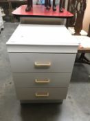 A white bedside 3 drawer unit with glass top