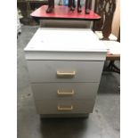 A white bedside 3 drawer unit with glass top