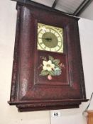 A carved wood framed wall clock with painted flower panel (Roman numeral clock face)