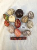 A box of stone eggs, painted wooden eggs, a wooden apple and a stone polyagonal paperweight.