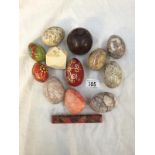 A box of stone eggs, painted wooden eggs, a wooden apple and a stone polyagonal paperweight.