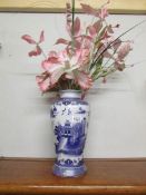 A blue and white willow pattern vase with silk flowers.